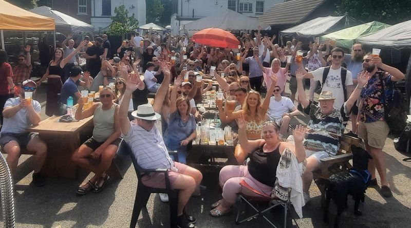 People cheering and waving their hands in a pub garden