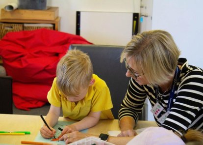 A child drawing with an adult sitting next to them