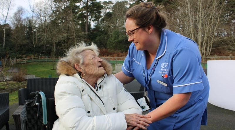 Phyllis Tuckwell nurse smiling with a patient in a wheelchair