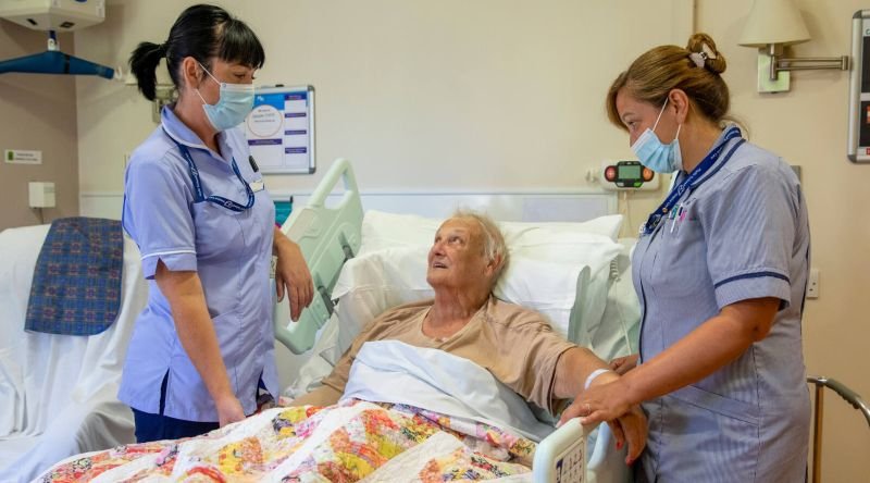 Two nurses helping a patient in bed
