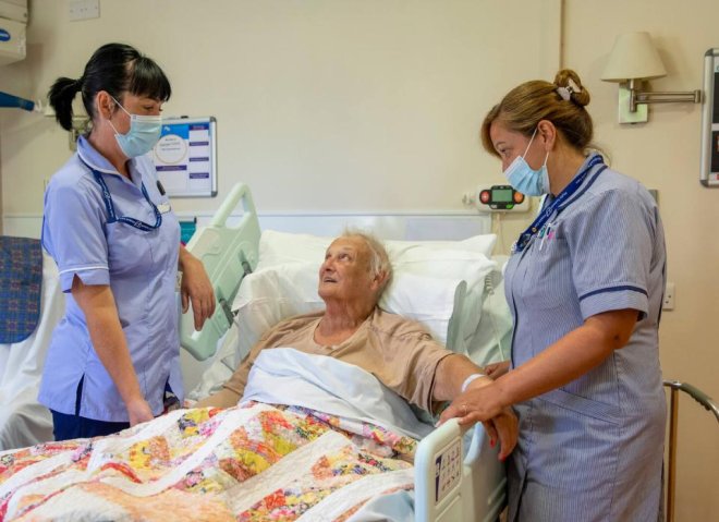 A patient in bed being looked after by two nurses
