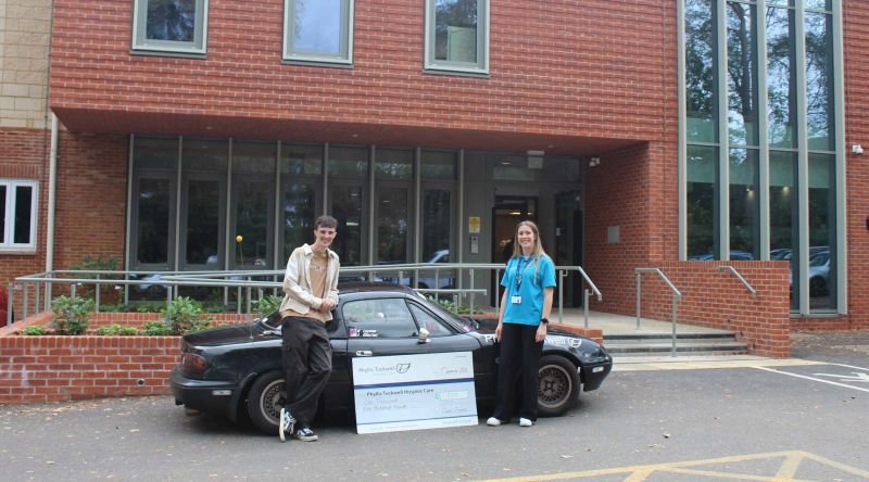 Two people in front of a car, with a big cheque