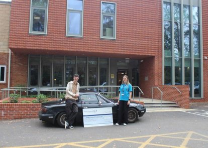 Two people in front of a car, with a big cheque