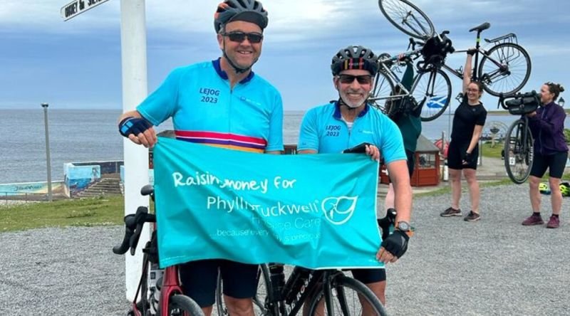 Two gentlemen on bicycles holding up a Phyllis Tuckwell banner