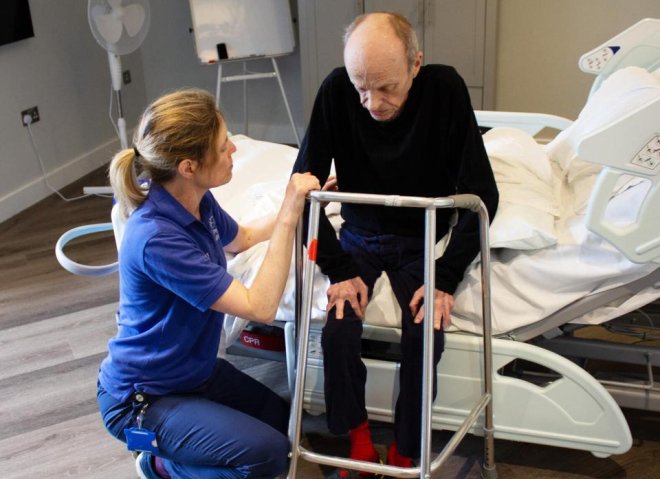 A Physiotherapist helping a patient walk with a frame