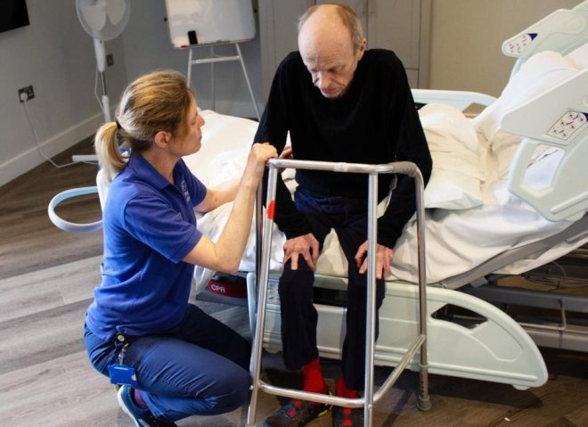 A Physiotherapist helping a patient walk with a frame