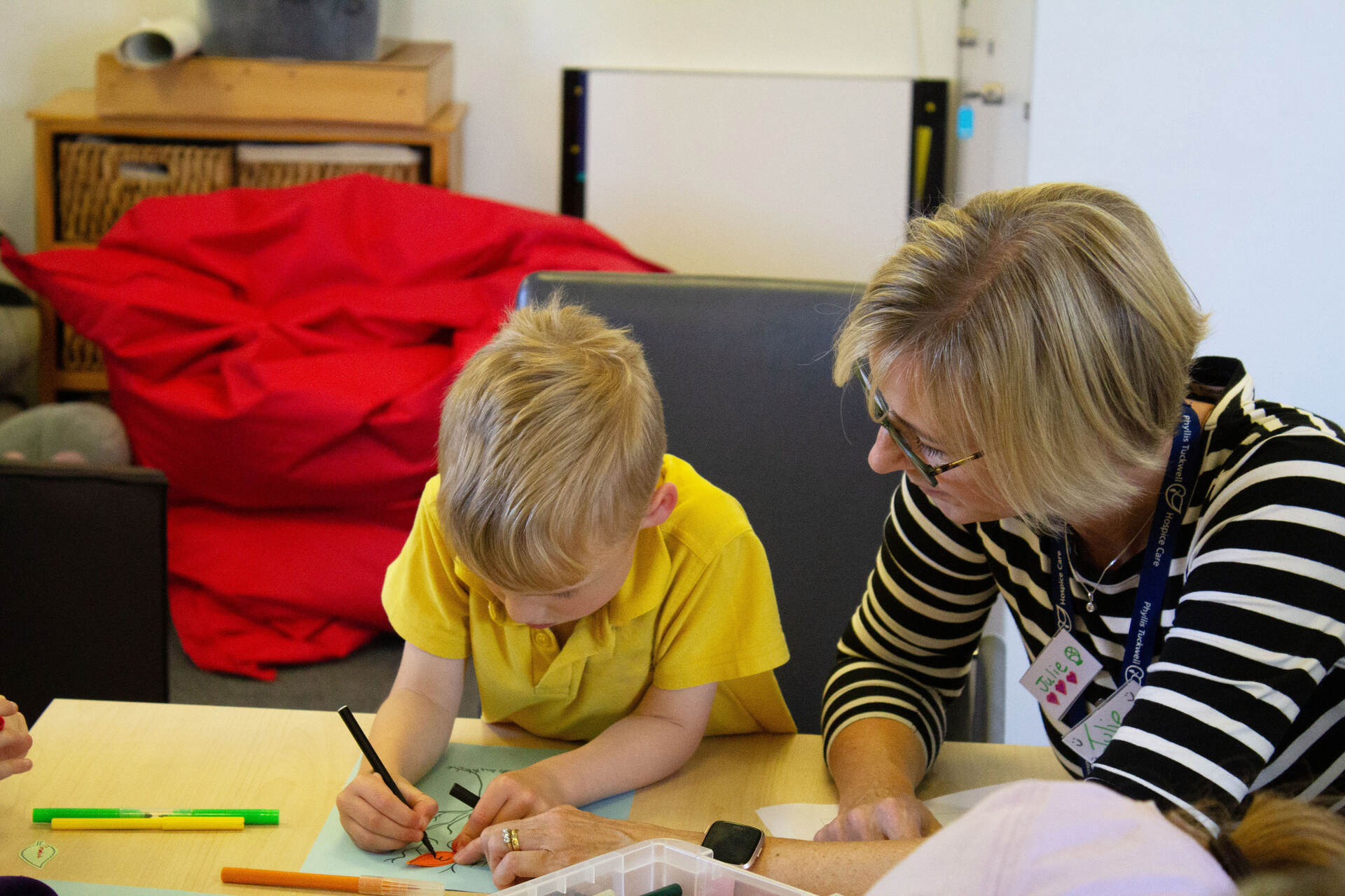 A child drawing with an adult sitting next to them