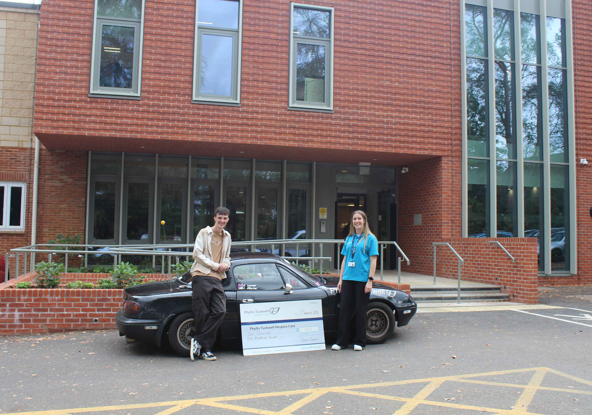 Two people in front of a car, with a big cheque