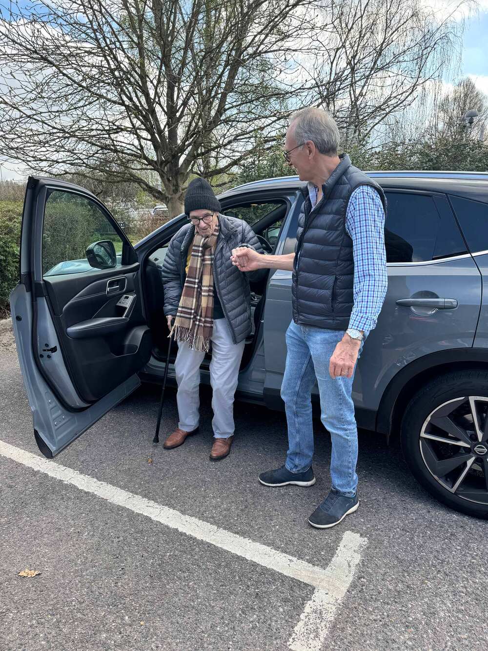 A patient and volunteer by a car